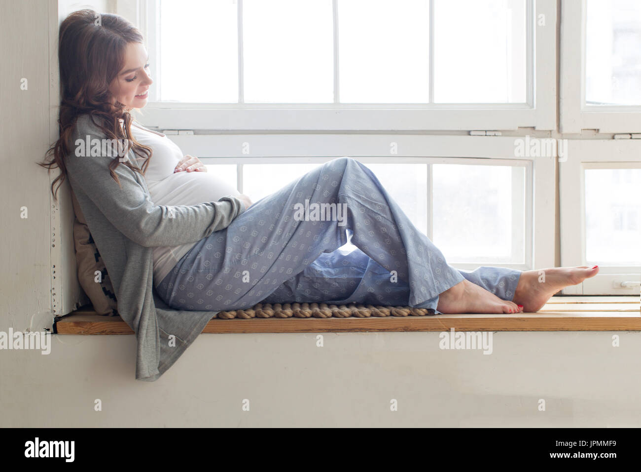 Donna incinta è seduta sul davanzale Foto Stock