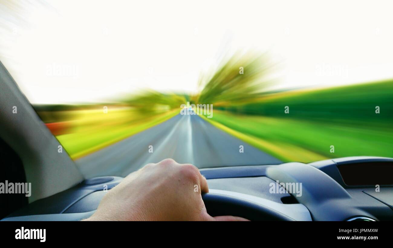 Prospettiva in prima persona del conducente dietro la ruota. Alla guida di una vettura veloce ad alta velocità con sfocate strada anteriore. Foto Stock