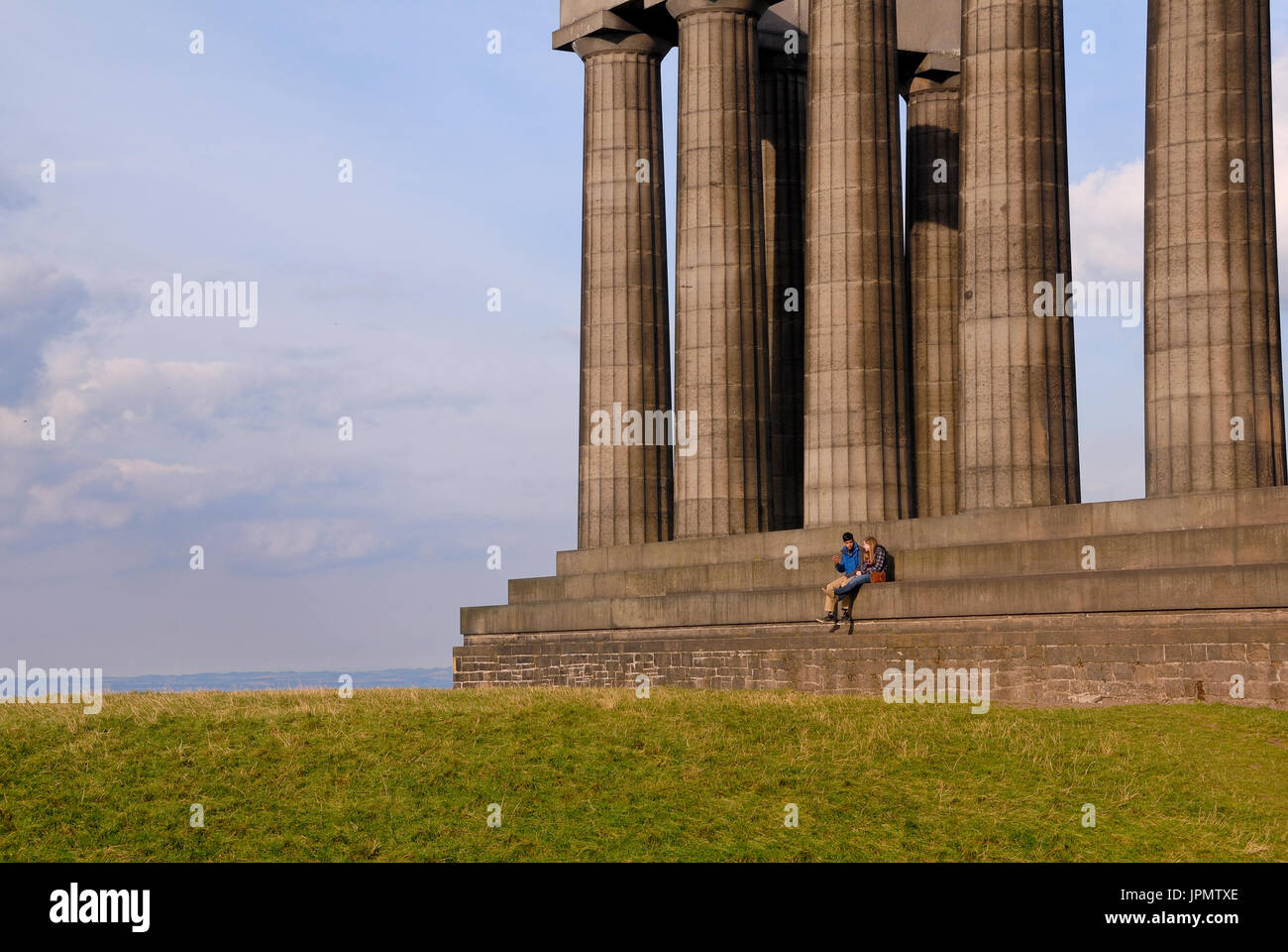 Un giovane seduto al monumento nazionale di Edimburgo. Il Monumento Nazionale di Scozia è un mezzo finito monumento sulla sommità del Carlton Hill. Foto Stock