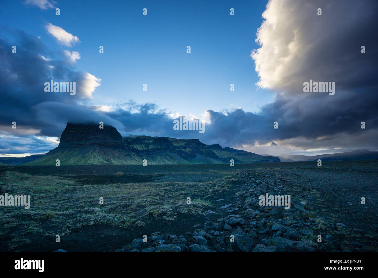 Islanda - Shining nuvole appeso su verdi montagne vulcaniche dietro il campo di lava Foto Stock