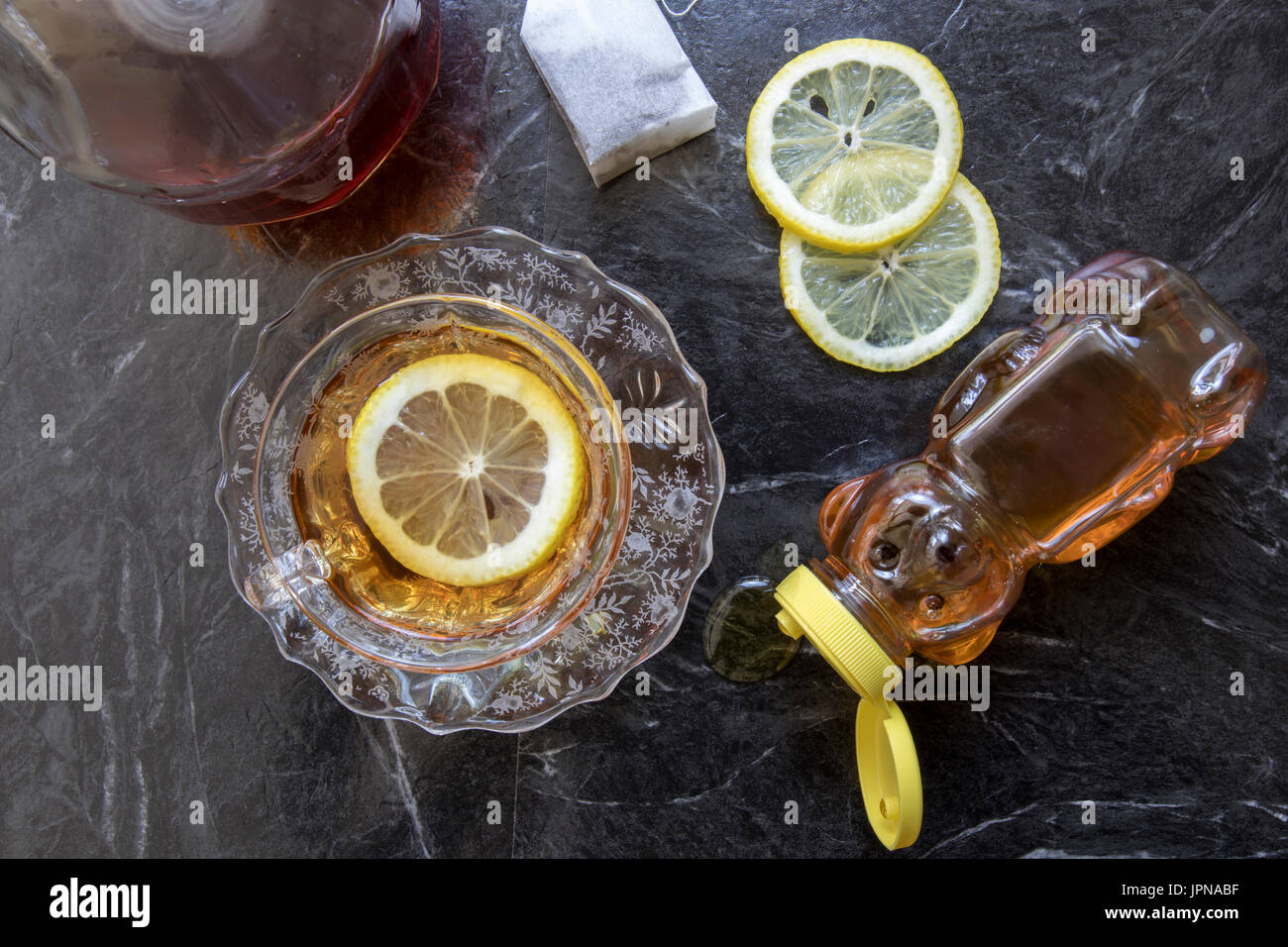Tazza classica di hot toddy cocktail in coppa di cristallo e il piattino con il miele, le fette di limone e un sacchetto da tè nero. Foto Stock