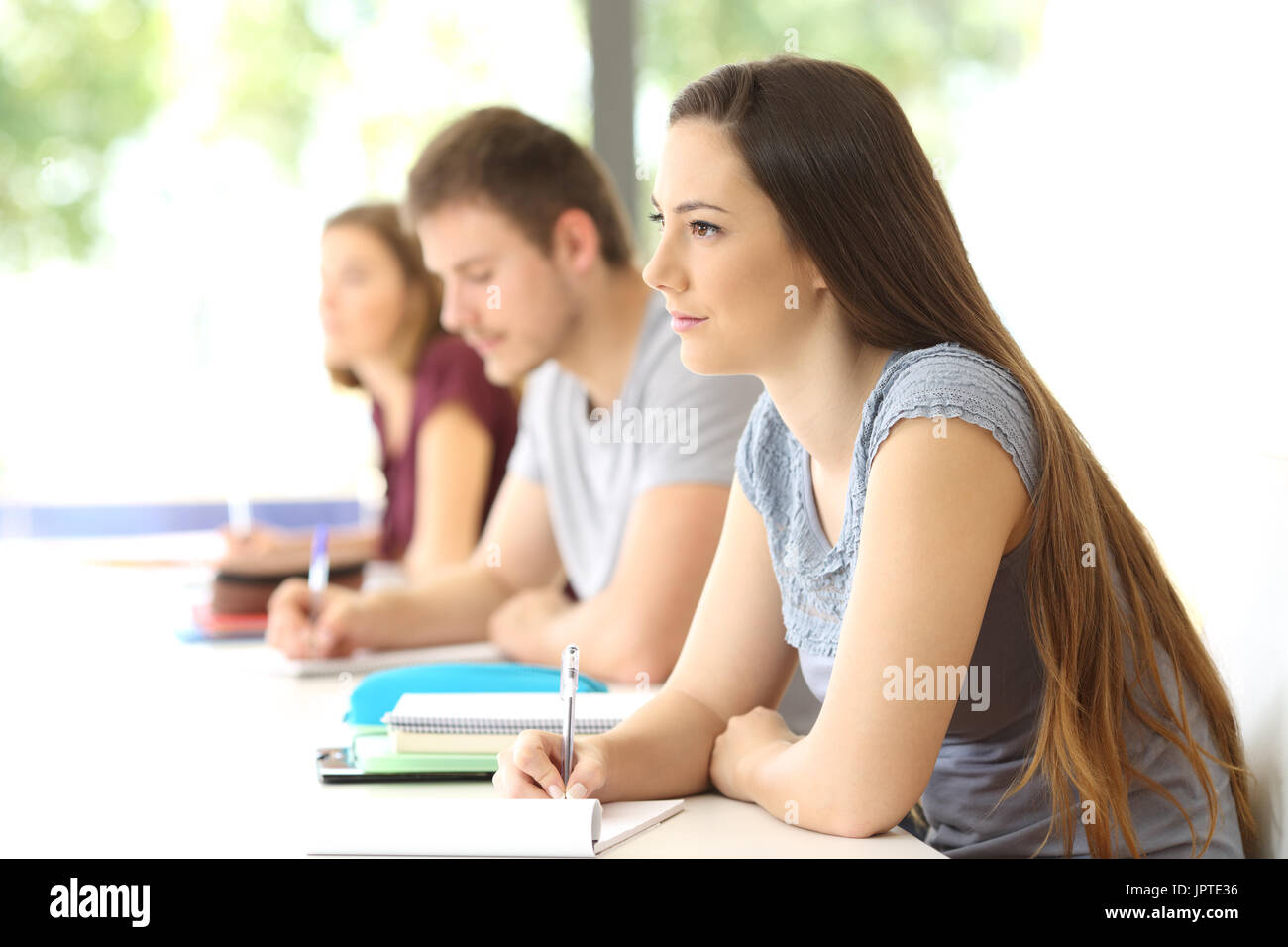 Lo studente ascolta una lezione in aula con altri compagni di classe in background Foto Stock