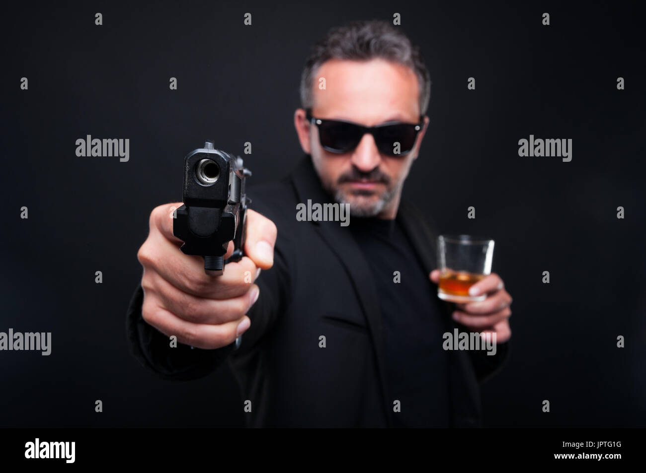 I Gangster uomo che ha di mira con la pistola alla fotocamera e bere whisky raffinati Foto Stock