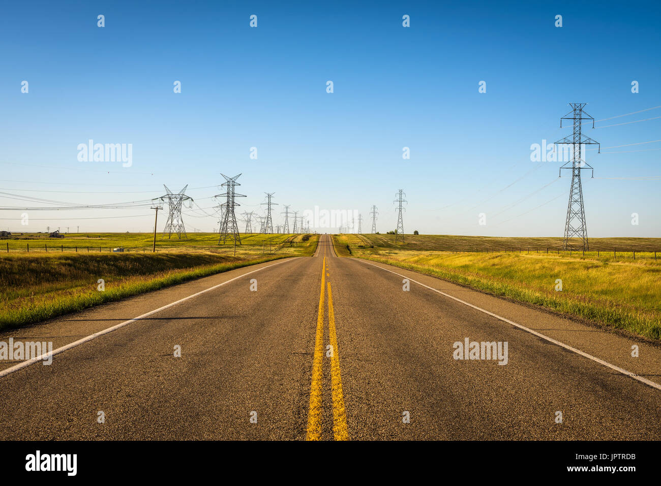 Ad alta energia elettrica pilastri con , linee di trasmissione lungo una strada vuota in Alberta, Canada Foto Stock