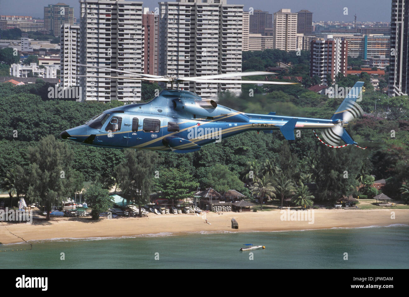 Bell 430 battenti lungo il tragitto su una spiaggia di sabbia e alberi verdi con grattacieli dietro Foto Stock