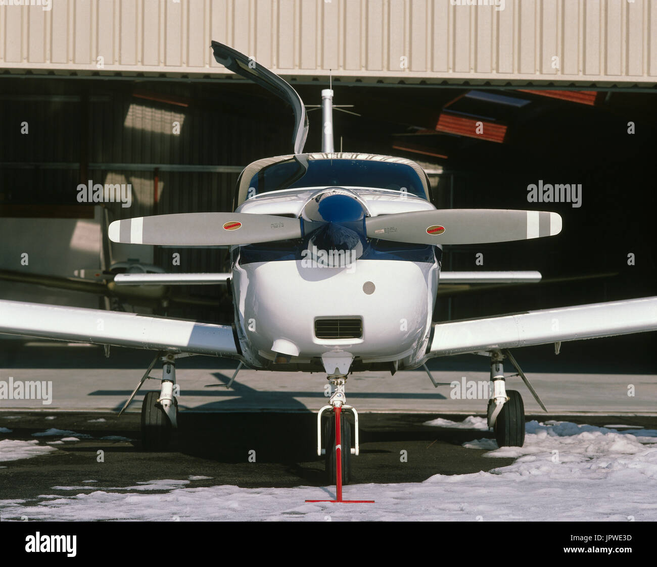 TB-20 parcheggiata di fronte hangar a neve con elica arrestato orizzontalmente con un blu spinner e apertura porta laterale e di una barra di traino sulla ruota anteriore unde Foto Stock
