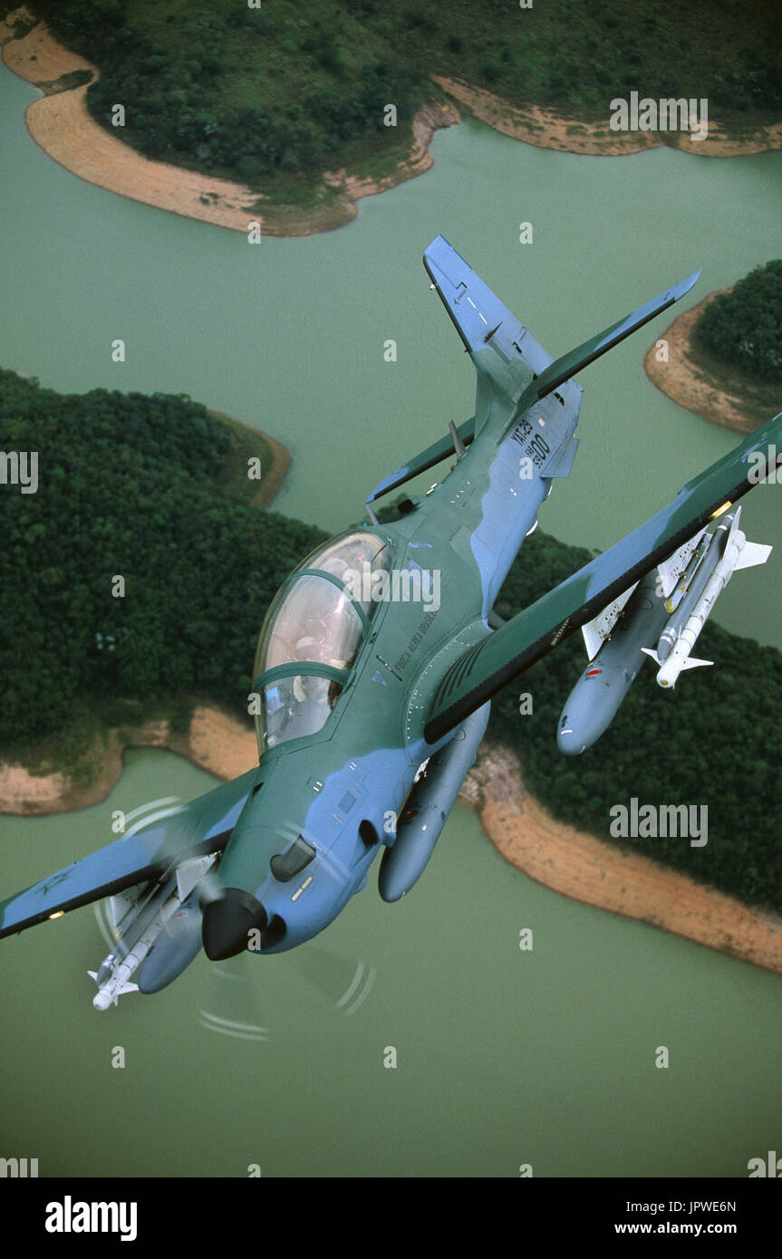 Forza aerea brasiliana Embraer EMB-314 Super Tucano banking oltre il fiume e gli alberi Foto Stock