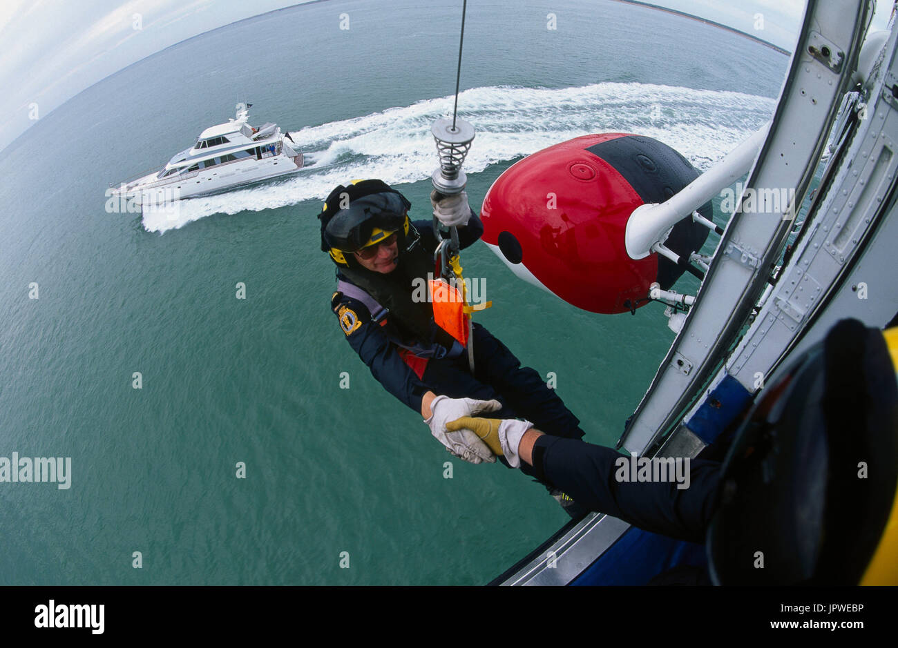 L'uomo nel cavo su di un cavo da un verricello su un HM Coastguard Sikorsky S-61N sorvolando un motoscafo a un aria-mare esercitazione di soccorso, servizio gestito da Br Foto Stock