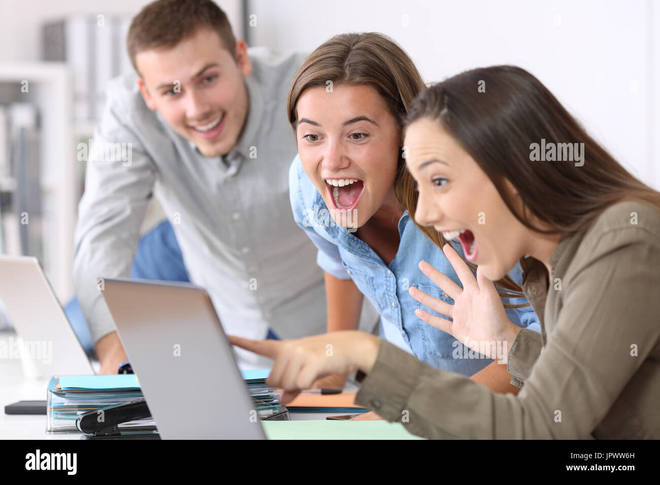 Tre dipendenti eccitati ricevendo buone notizie on line in ufficio Foto Stock