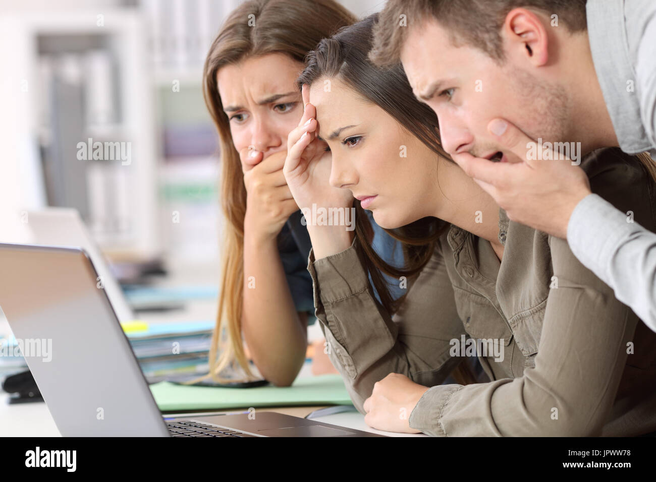 Tre dipendenti preoccupati la lettura di cattive notizie sulla linea in un notebook in ufficio Foto Stock