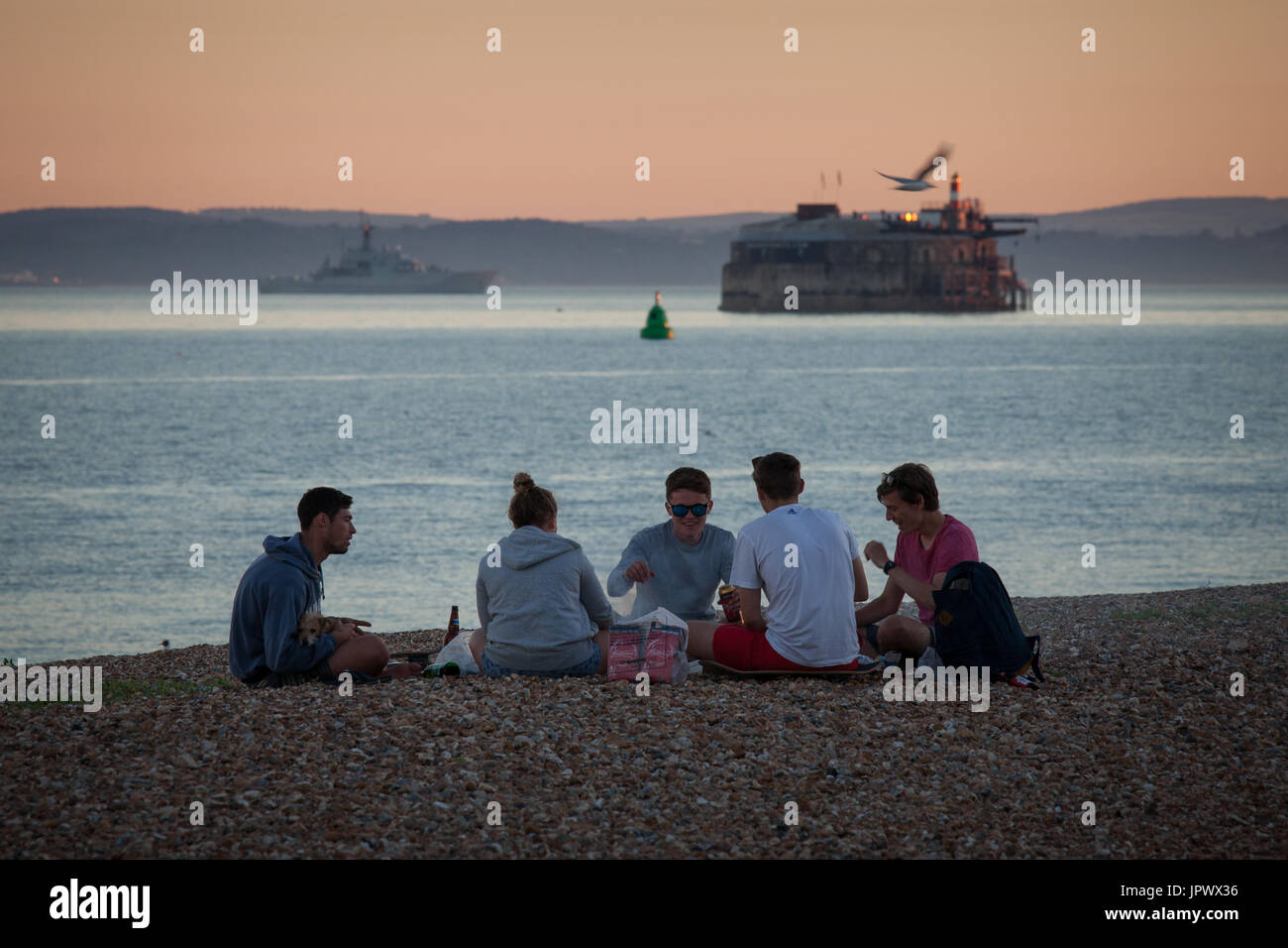 Un gruppo di giovani adulti all'aperto socializzare e gustare drink e un barbecue sulla spiaggia a Southsea, Portsmouth. Foto Stock