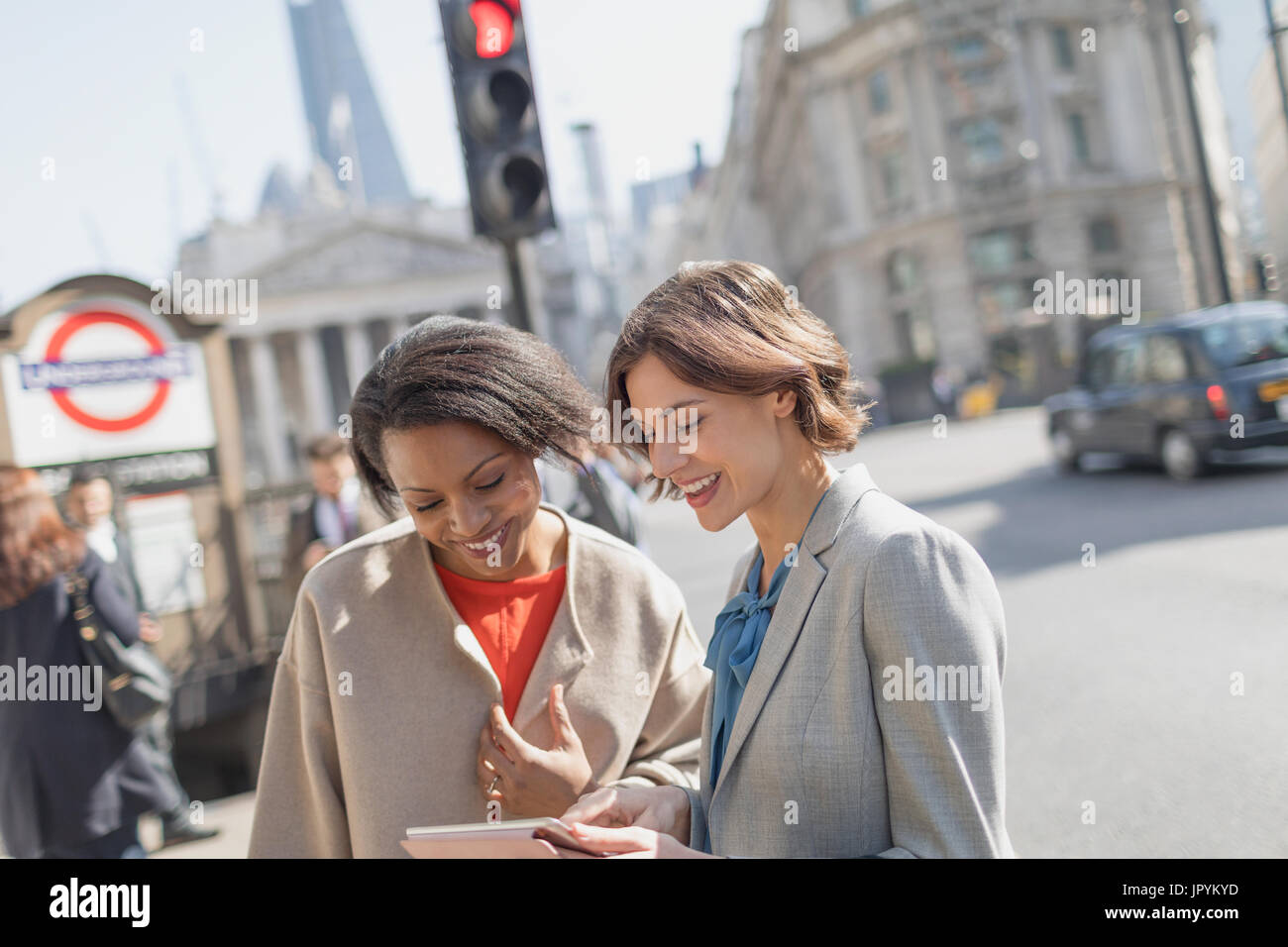 Imprenditrici sorridente con tavoletta digitale parlando sulla soleggiata città urban street Foto Stock