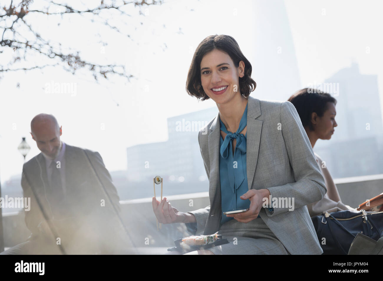 Ritratto sorridente imprenditrice mangiare sushi in pausa pranzo nel soleggiato parco urbano Foto Stock