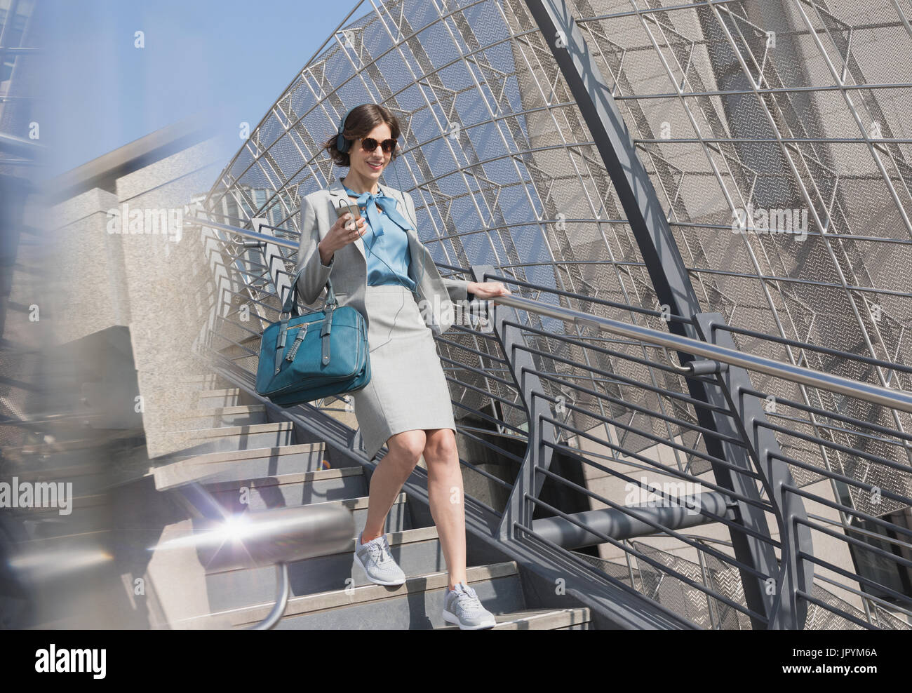 Imprenditrice in scarpe da ginnastica con un telefono cellulare e cuffie soleggiata discendente scale urbana Foto Stock