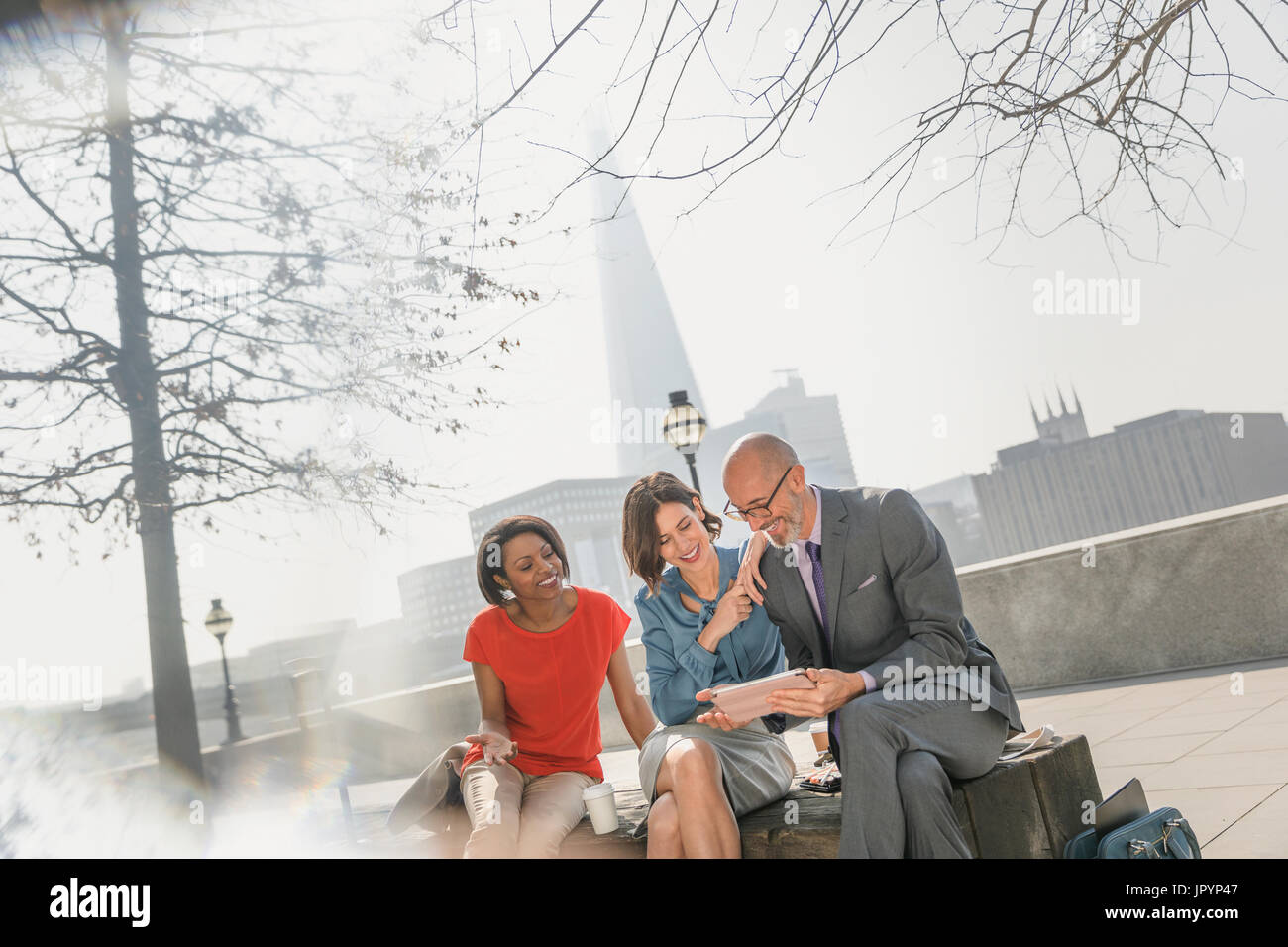 La gente di affari incontro, utilizzando digitale compressa nel soleggiato parco urbano, London, Regno Unito Foto Stock