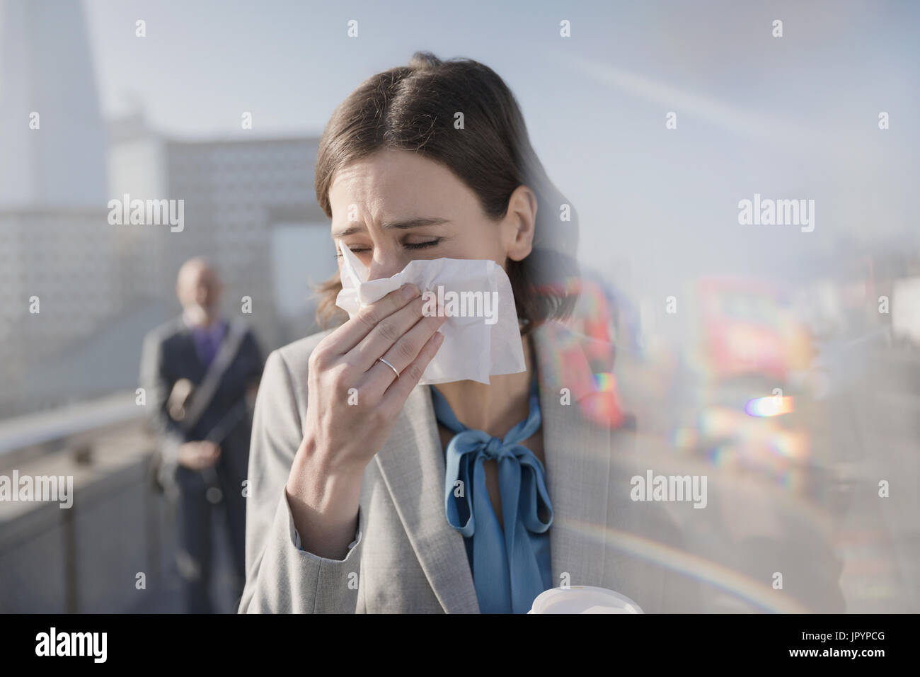 Imprenditrice con allergie soffia il naso nel tessuto sulla soleggiata marciapiede urbano Foto Stock