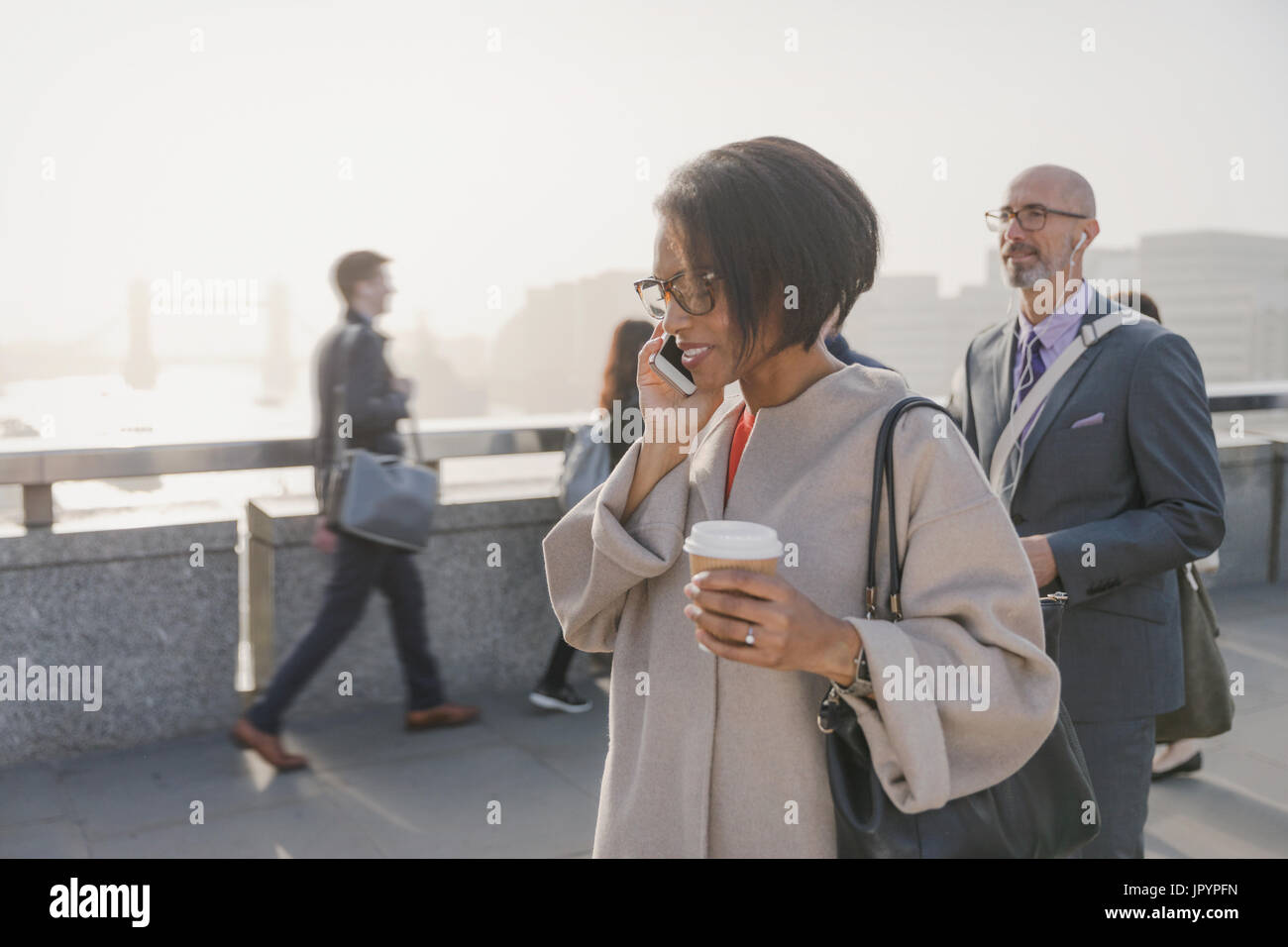 Silhouette imprenditrice parlando al cellulare e di bere il caffè sul ponte urbano, London, Regno Unito Foto Stock