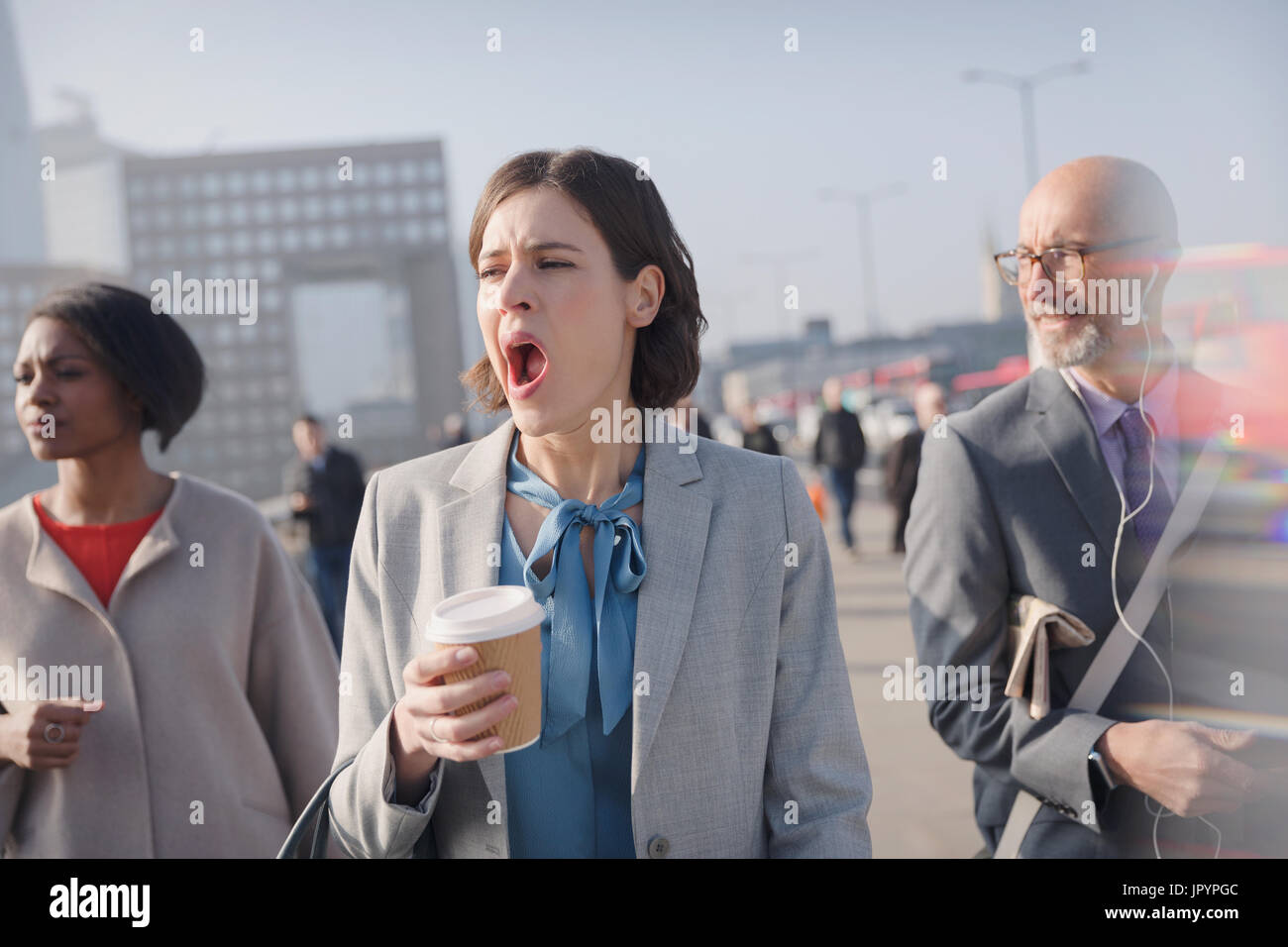 Stanco imprenditrice con caffè sbadigliare sulla mattina di sole urbano ponte pedonale Foto Stock