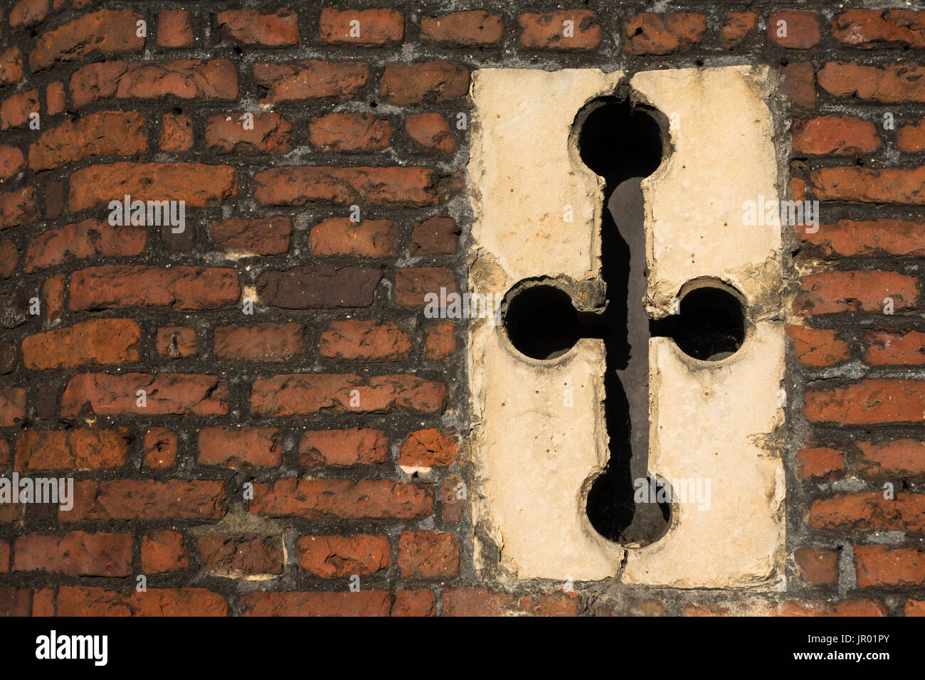 Close-up di dettaglio a forma di croce finestra fessura freccia in Tudor architettura rosso esterno muro di mattoni Foto Stock