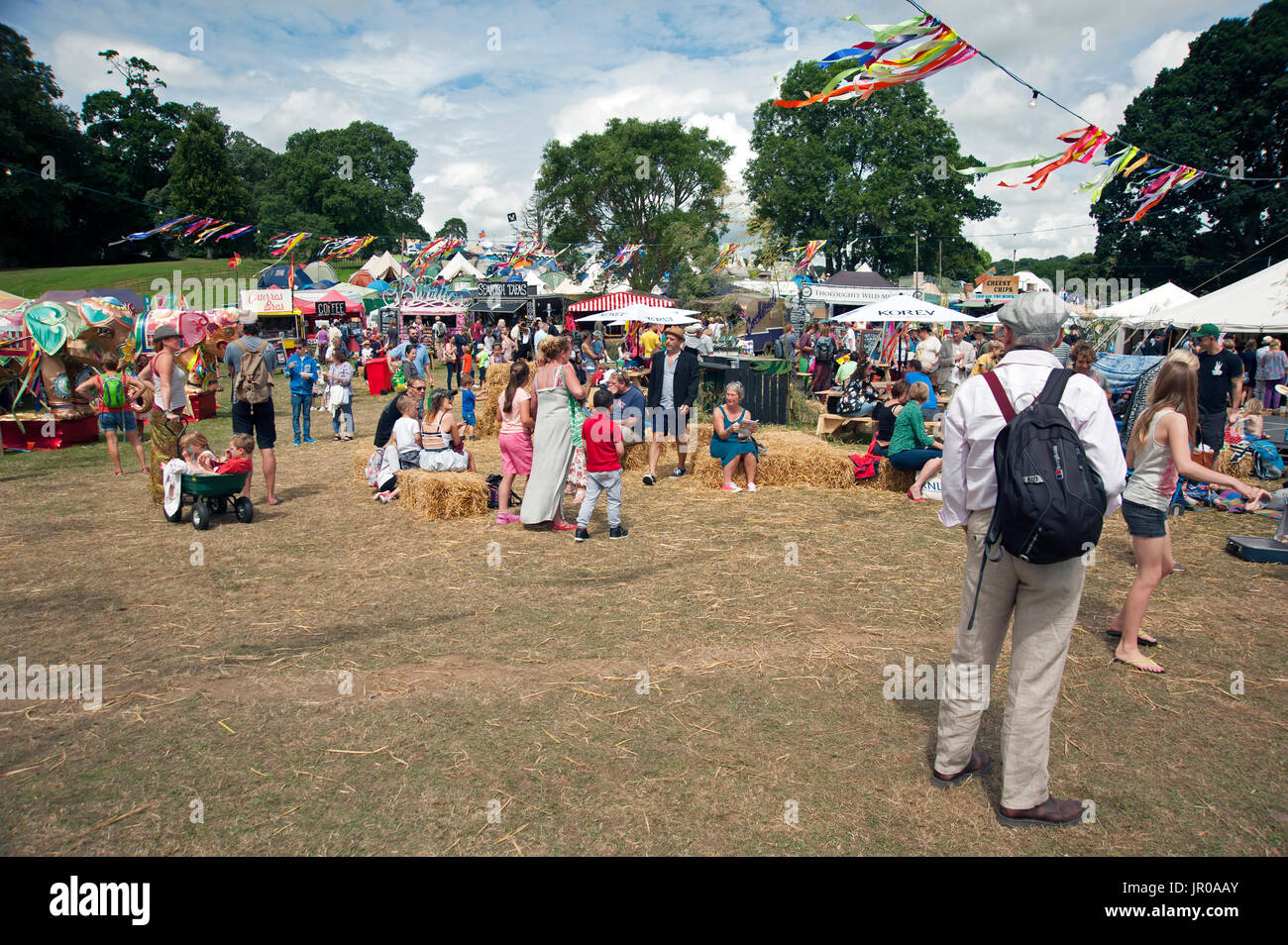 Famiglie godere il sole seduti a bere e mangiare fuori tende e tabelloni elettronici al porto Eliot Festival Cornwall Regno Unito Foto Stock