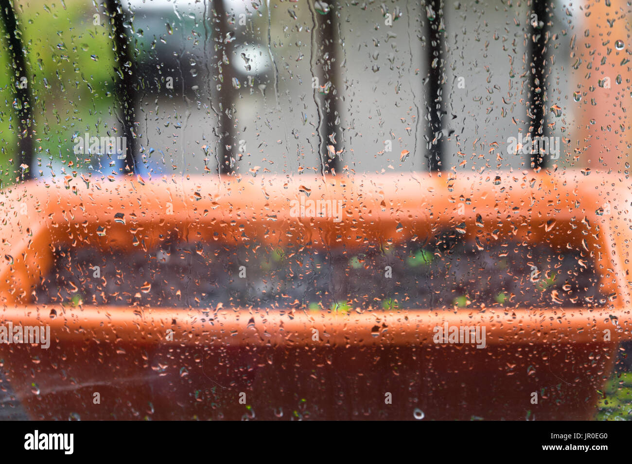Rettangolare di color terracotta pentola floreale al di fuori su di un balcone durante la pioggia - Concetto di pioggia Foto Stock