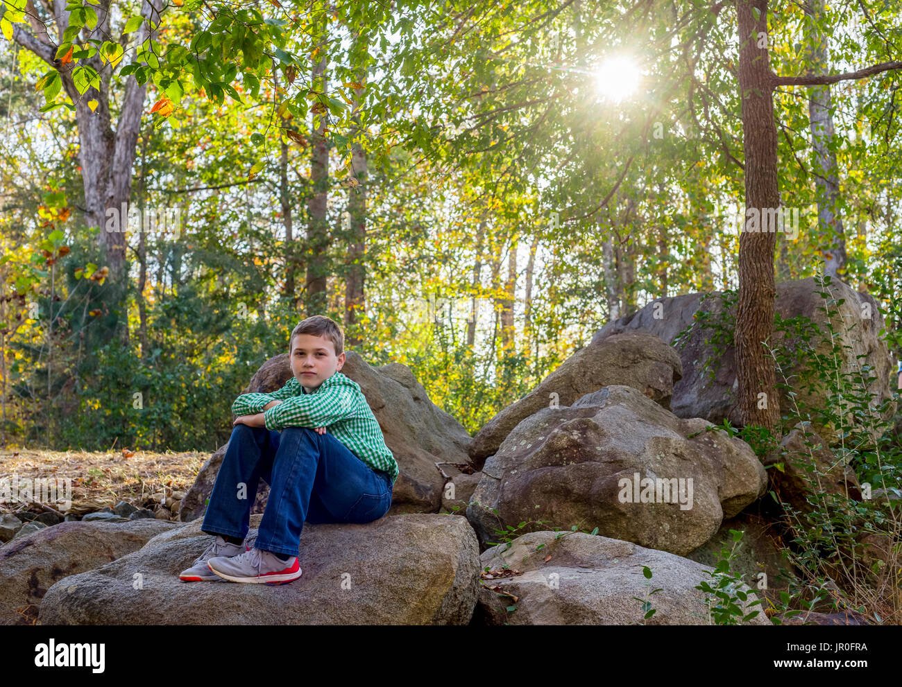 Un giovane ragazzo caucasico siede su massi su Cedar Grove Road; Pittsboro, North Carolina, Stati Uniti d'America Foto Stock