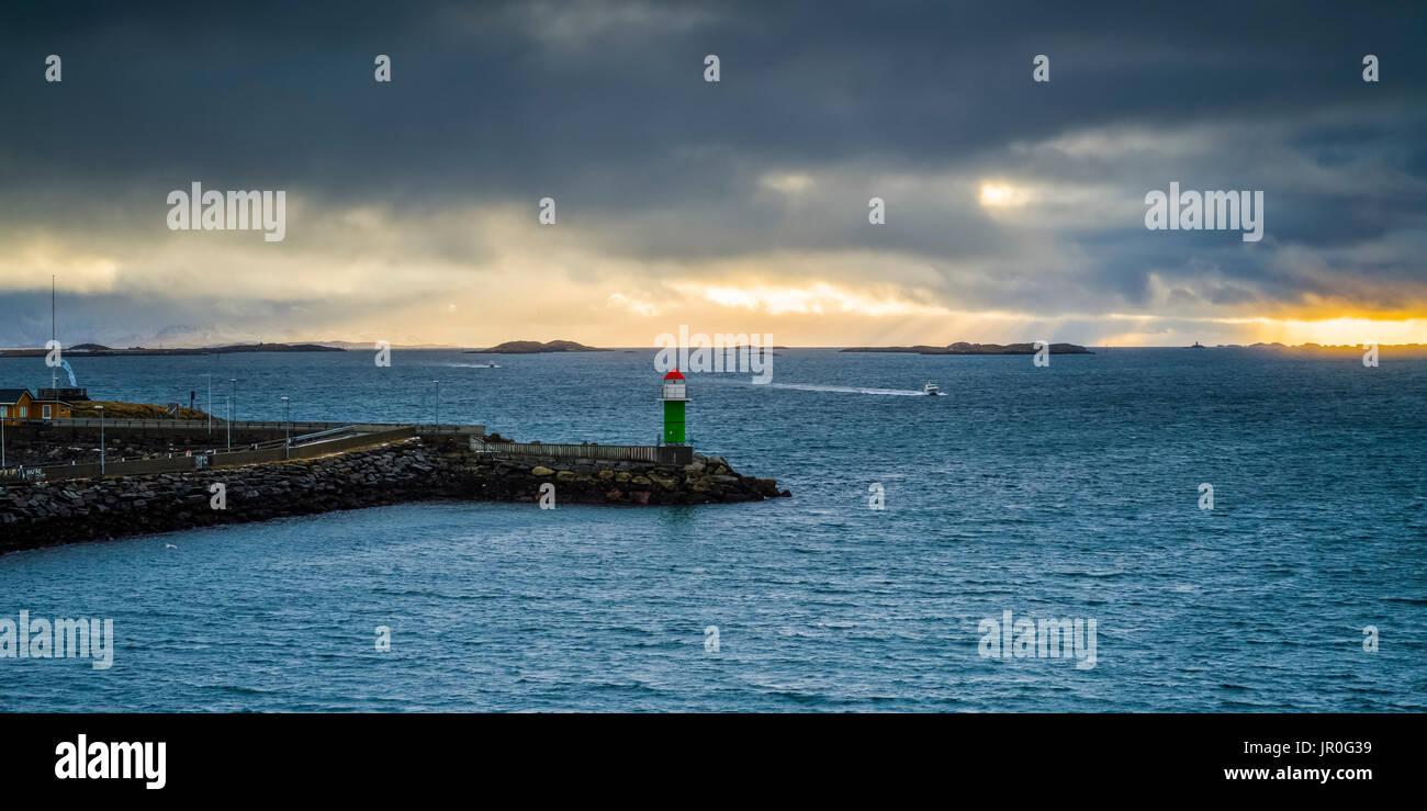 Un faro si siede sul bordo dell'acqua con un dorato tramonto sul mare sotto le nuvole; Nordland, Norvegia Foto Stock