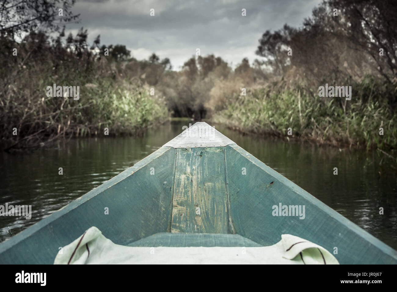 Prua della barca con direzione di avanzamento verso la banca sul fiume nel giorno nuvoloso con drammatica cielo simboleggiano in avanti Foto Stock