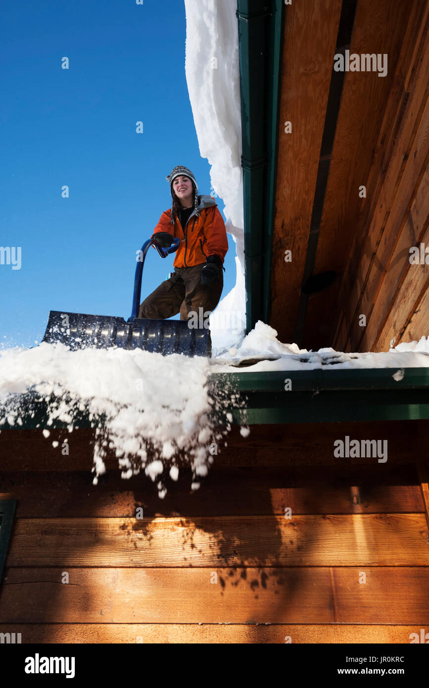 Una giovane donna rimuove la neve dal tetto della sua casa; Omero, Alaska, Stati Uniti d'America Foto Stock