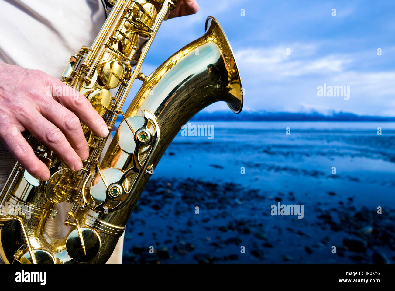 Un uomo sta giocando un sassofono sulla spiaggia al bordo dell'acqua; Alaska, Stati Uniti d'America Foto Stock