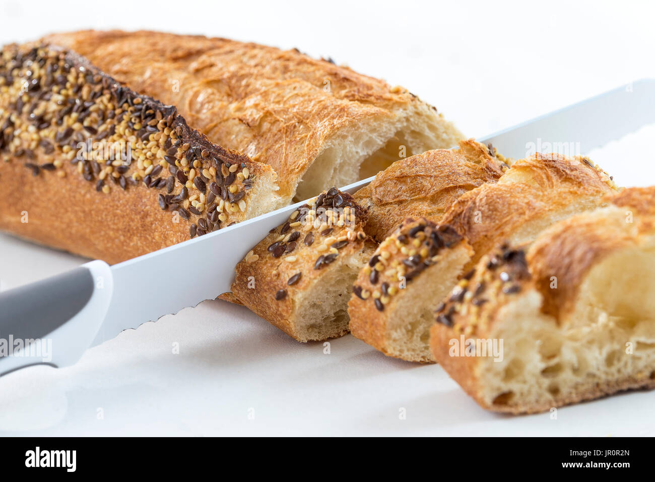 Primo piano di una baguette bianca guarnita con semi diversi, come ad esempio il sesamo e semi di papavero, tagliati su sfondo bianco Foto Stock