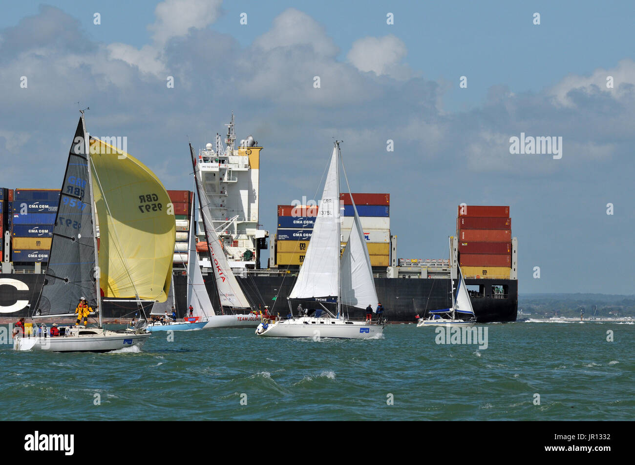 Un contenitore grande nave che entra in porto di Southampton o porto durante la cowes week vicino ad alcuni racing yachts off dell' isola di Wight sul mare solent Foto Stock