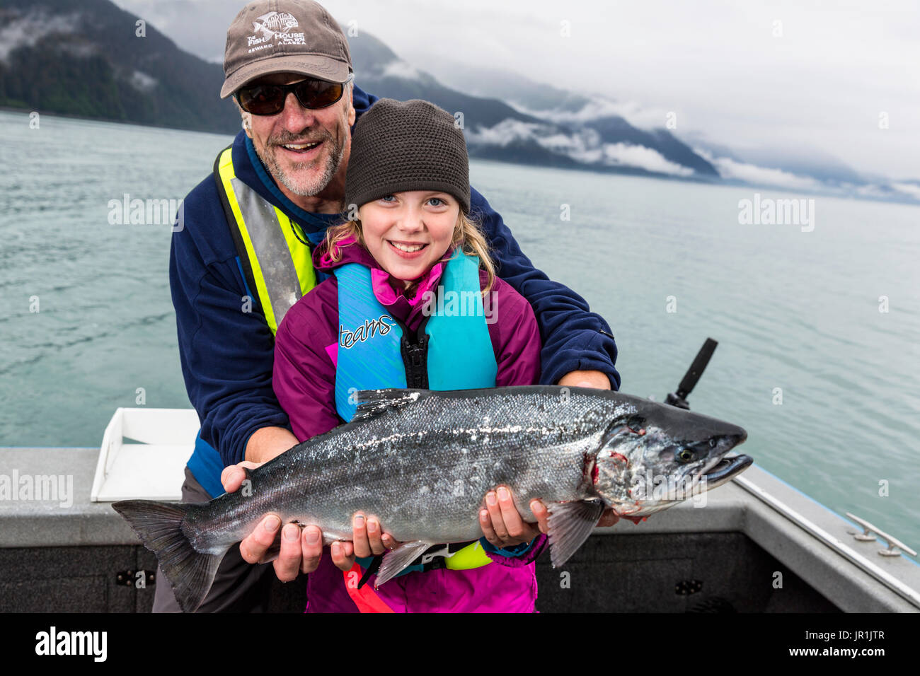 Padre e figlia tenendo in mano un salmone argento mentre su una barca, Seward, centromeridionale Alaska, STATI UNITI D'AMERICA Foto Stock