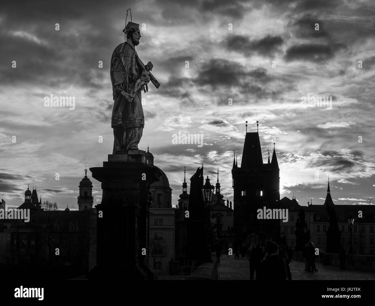 Statua di un uomo sul Ponte Carlo con stagliano palazzi sotto un cielo nuvoloso; Praga, Repubblica Ceca Foto Stock
