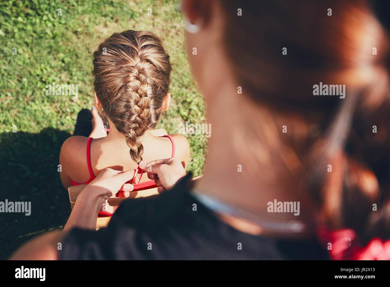 Giovane donna rendendo trecce di capelli della bambina sul giardino in campagna. Foto Stock