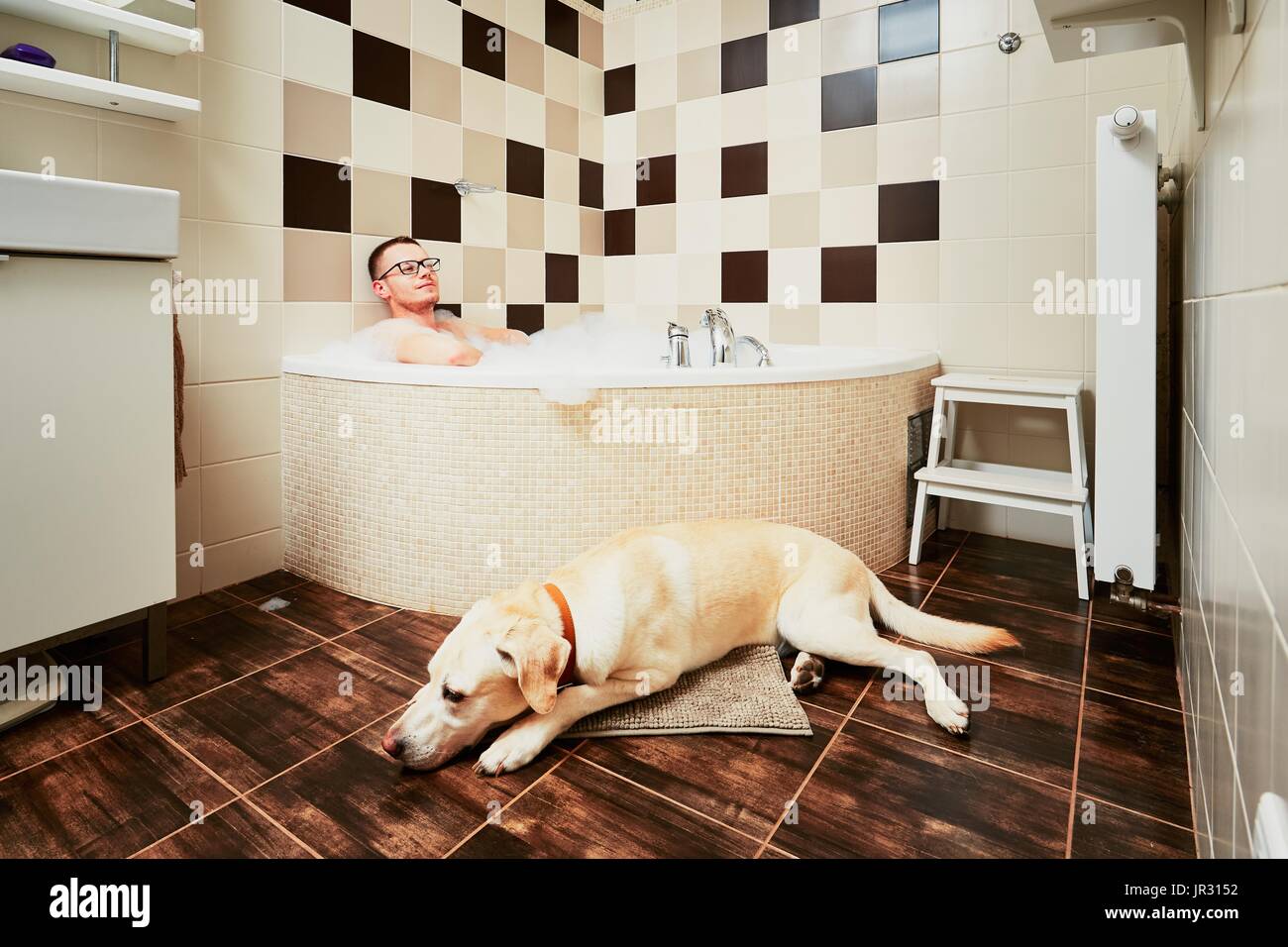 Vivere con il cane. Giovane uomo relax nel bagno con il suo giallo labrador retriever. Foto Stock