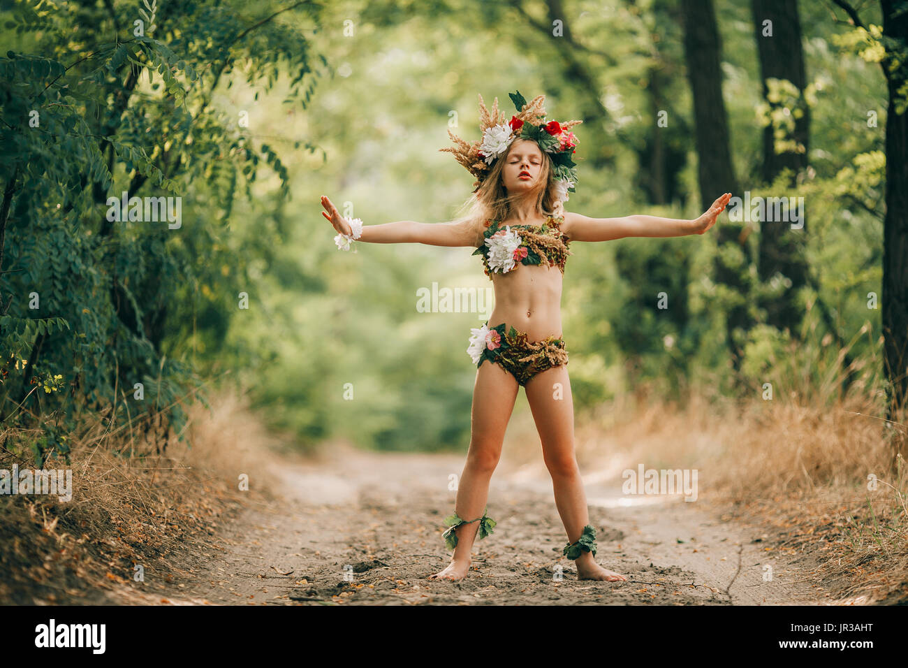 Bellissima bambina in immagine della ninfa dryad con testa floreale corona sorge in una strada forestale e l'incantesimo. Foto Stock