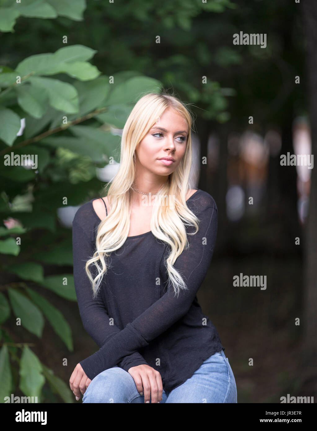 Bella bionda diciannovenne ragazza seduta in un giardino Foto Stock