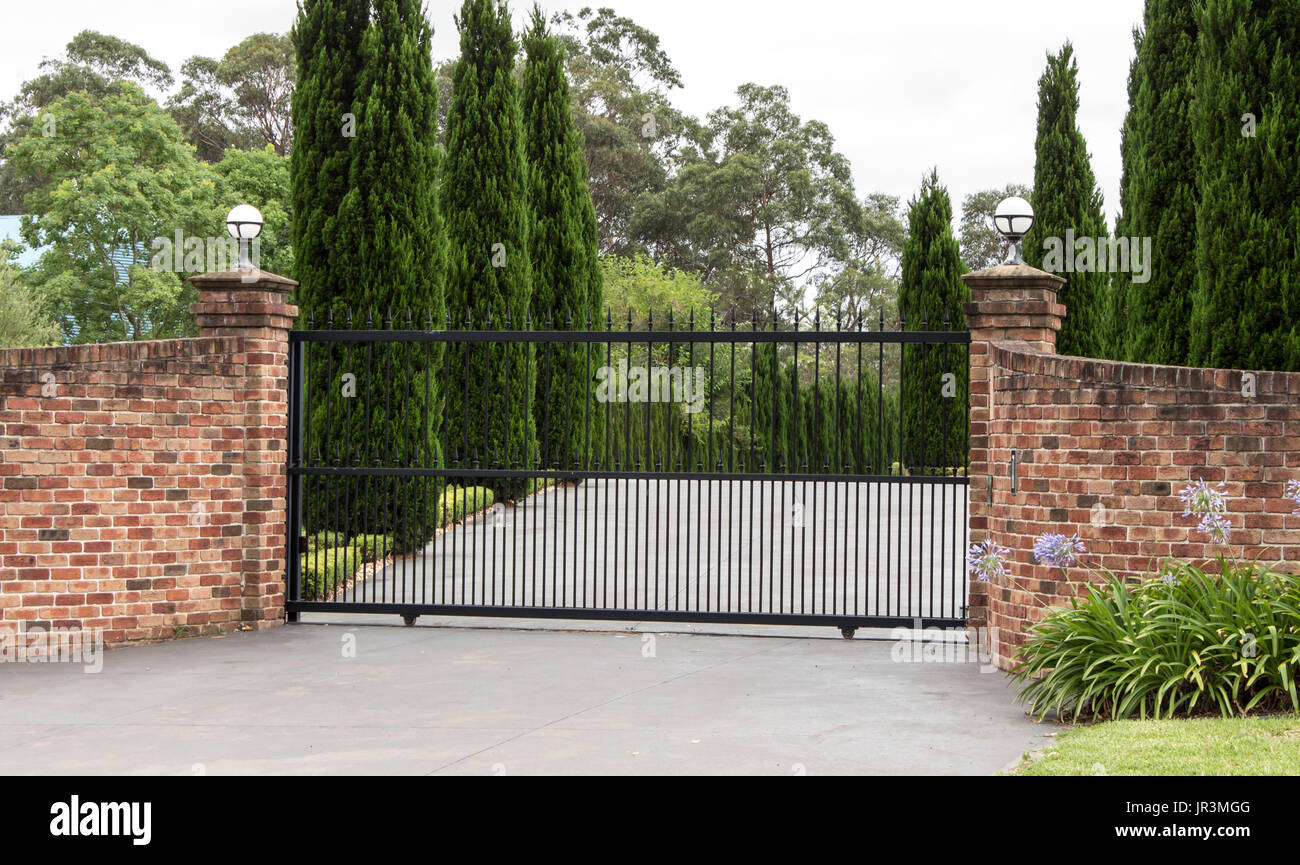 Viale di metallo cancelli di ingresso impostato nel recinto di mattoni con giardino di alberi in background Foto Stock