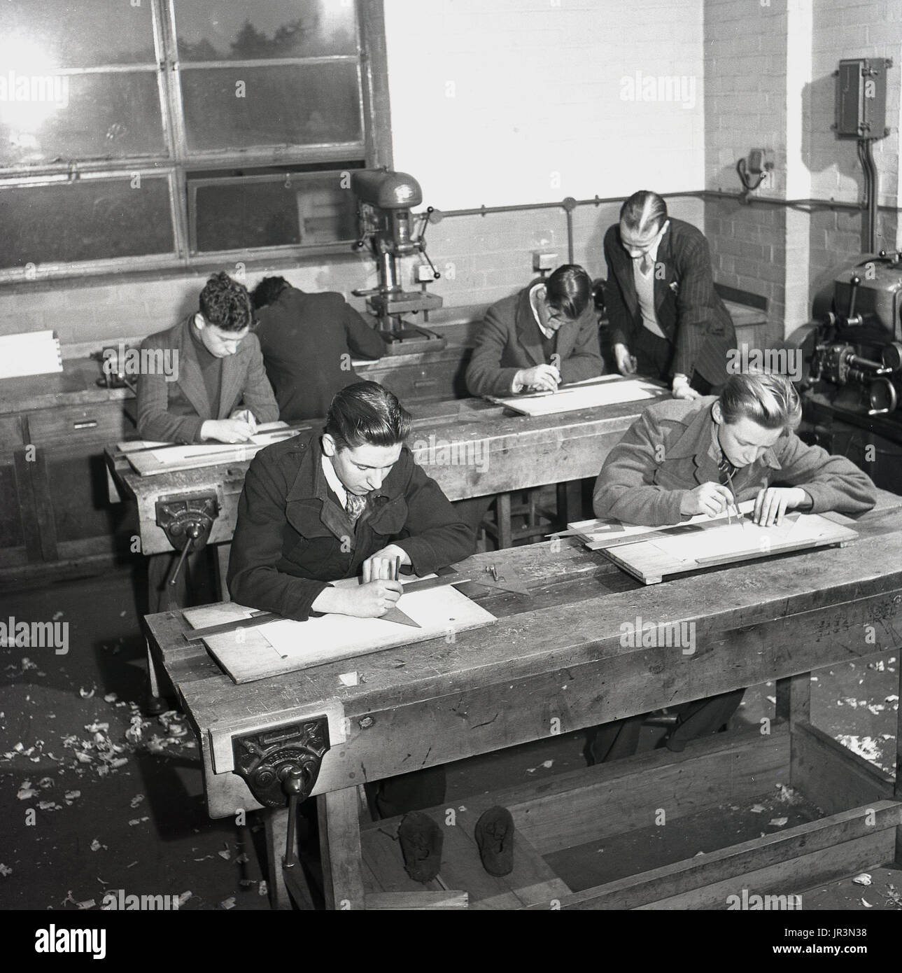 1948, Inghilterra, storico, immagine mostra mining apprendisti seduta in legno banchi di lavoro facendo da disegno o disegni tecnici con i righelli e della redazione di triangoli, sotto la supervisione di un maschio tuitor. Foto Stock