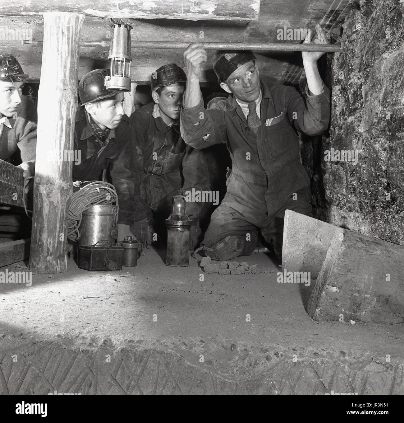 1948, storico, Inghilterra, adulti miner dimostrando ai maschi giovani apprendisti di data mining o apprendisti tecniche di data mining, usando un palo di legno per controllare la parete della miniera. Foto Stock