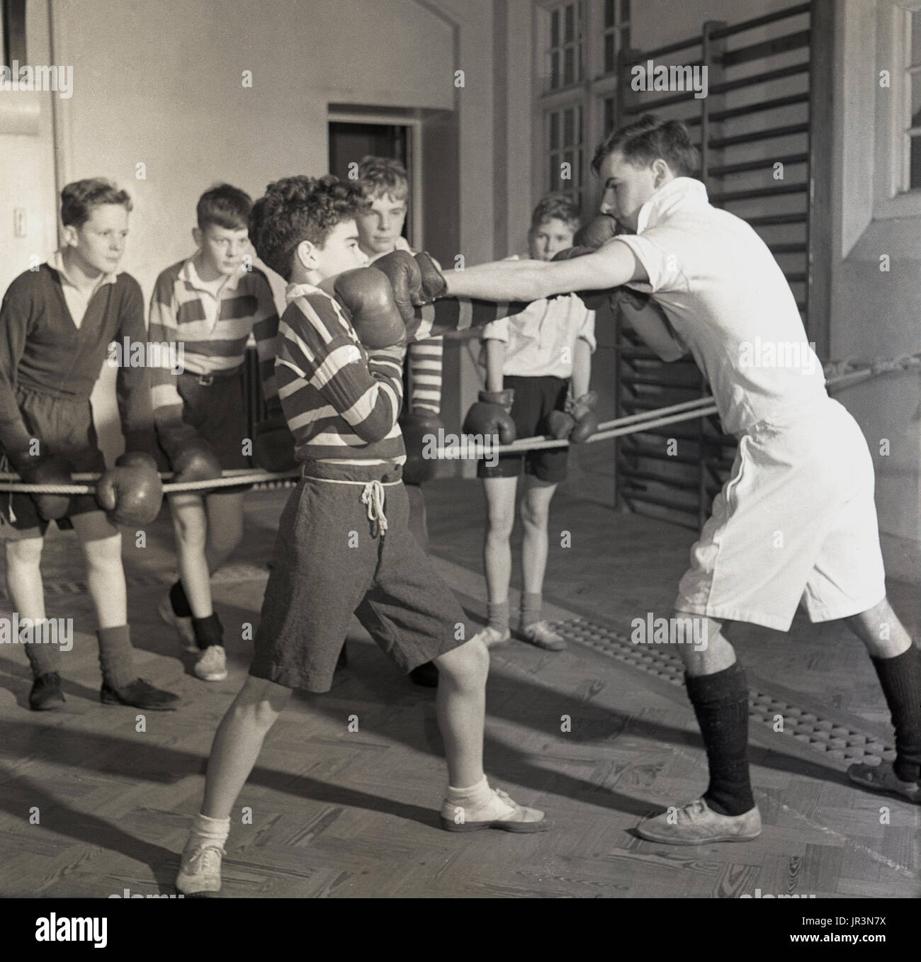 1948, Inghilterra, un giovane ragazzo di scuola che viene insegnato difesa nello sport della boxe da un insegnante di sport maschile, mentre altri ragazzi guardano e imparano, Hailleybury Public School, l'unica scuola di imbarco di un ragazzo tradizionale britannico. Foto Stock