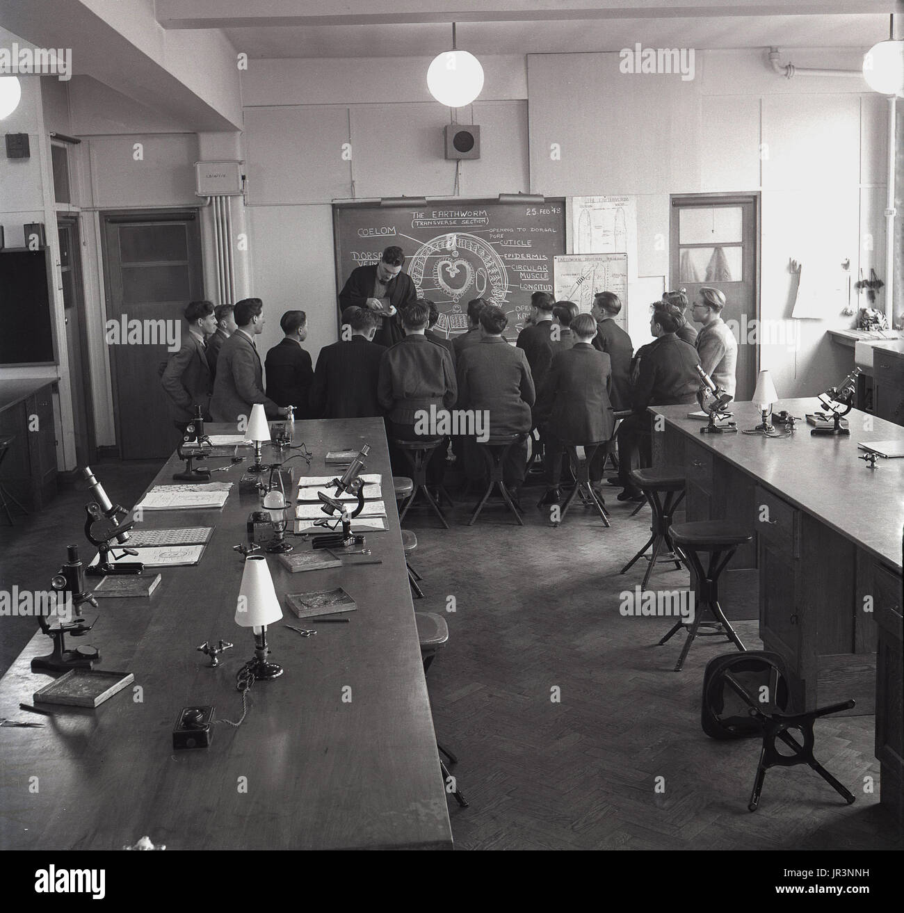 Degli anni Cinquanta, storico, scienza classe studiando i lombrichi, un gruppo di studenti di sesso maschile a sedersi su sgabelli di fronte alla classe dalla lavagna come insegnante mostra loro campioni, Inghilterra, Regno Unito. Foto Stock