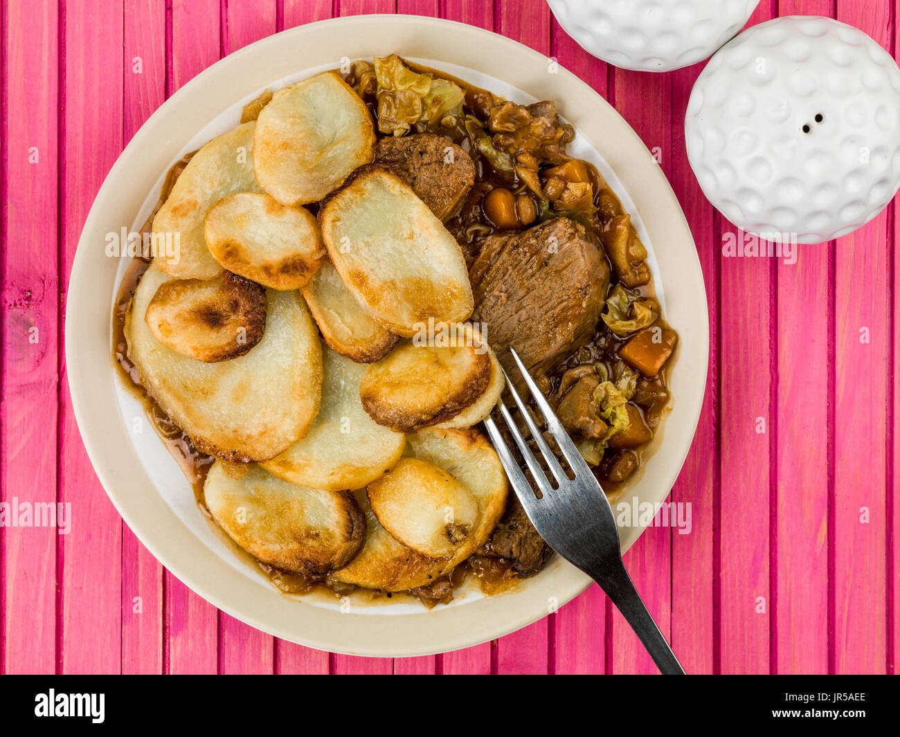 Agnello hotpot con fette di patate e cipolla con sugo di carne contro una rosa di sfondo di legno Foto Stock