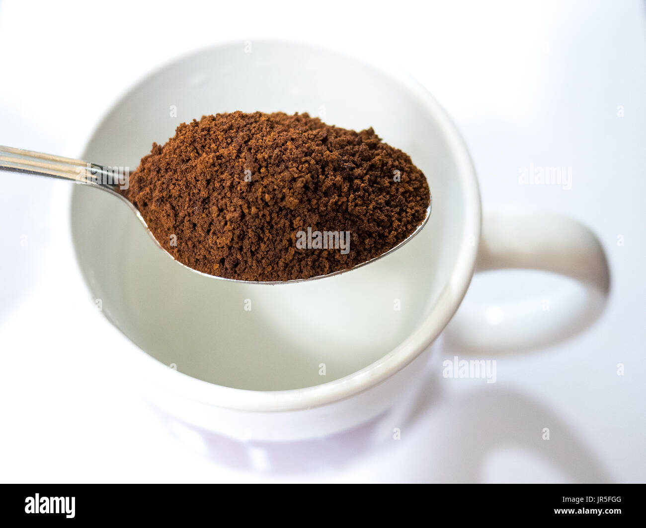 Il caffè istantaneo su un cucchiaio sopra una tazza di caffè Foto Stock