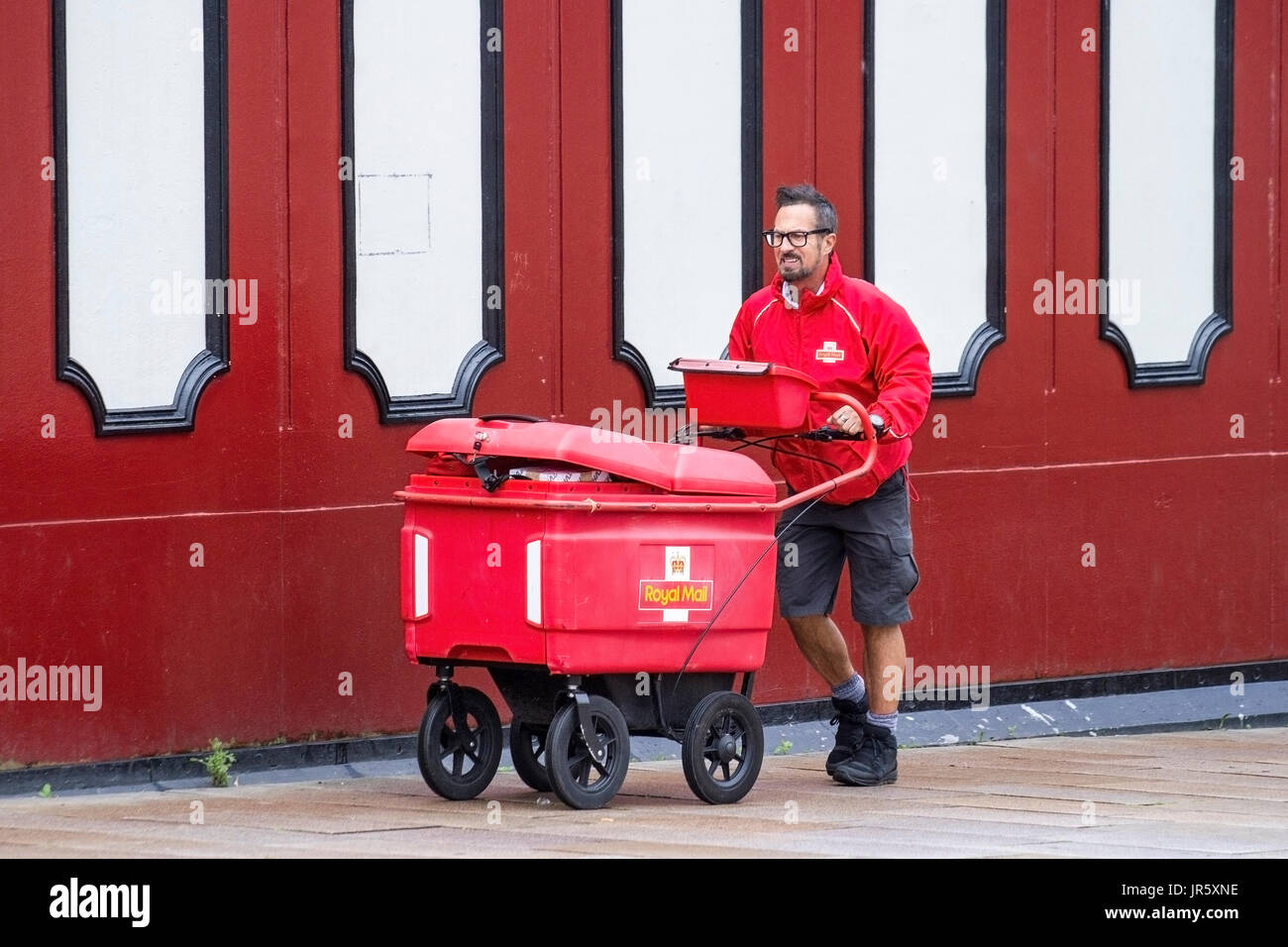 Royal mail Postman con grande buggy con ruote per pacchi pieni, che consegna la posta nel centro di Preston, Regno Unito Foto Stock