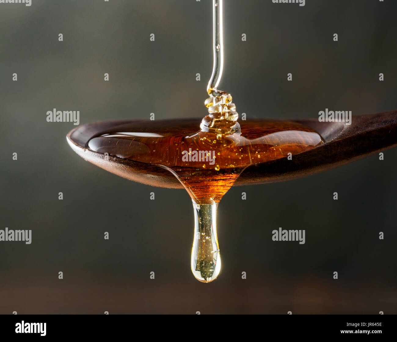 Il miele versando sul cucchiaio di legno e gocciolamenti dal cucchiaio. Sfondo scuro. Extreme close up. Foto Stock