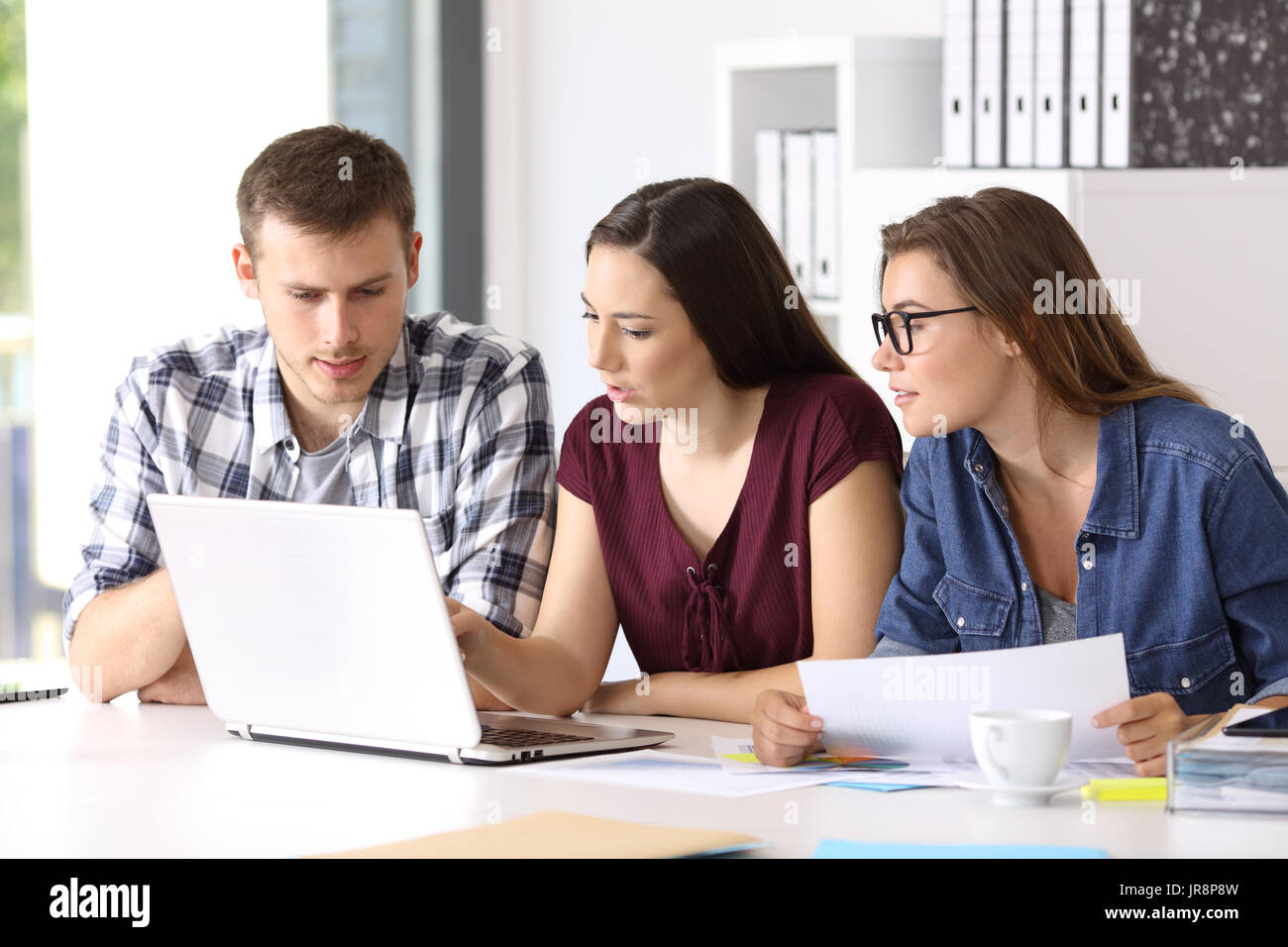Tre gli imprenditori coworking on line con un laptop seduto in un desktop in ufficio Foto Stock