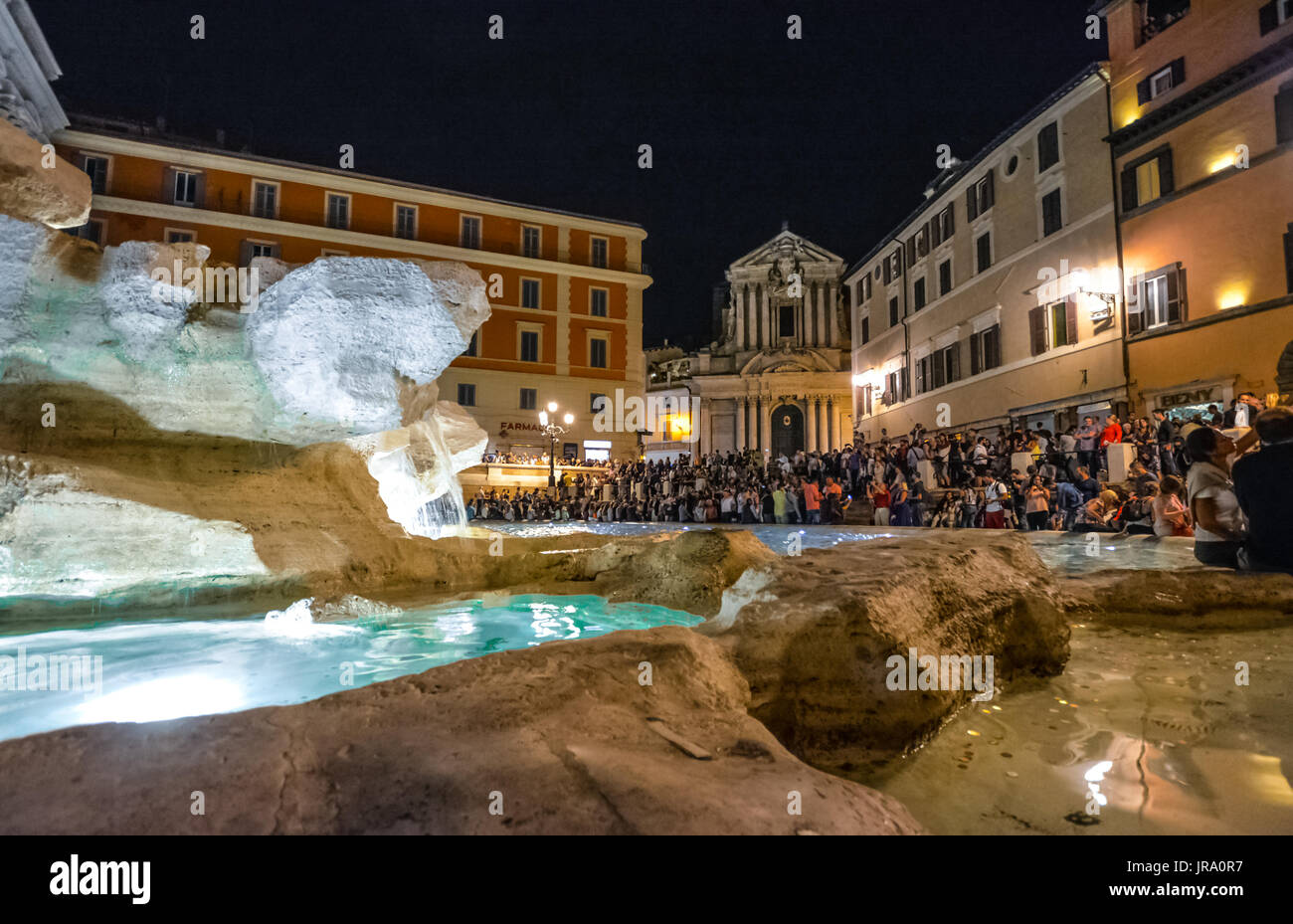 La folla di persone la sera presso la Fontana di Trevi con la chiesa in background in Roma Italia Foto Stock