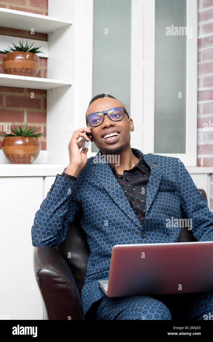 Giovane uomo d affari di parlare sul suo cellulare con un computer portatile aperto Foto Stock